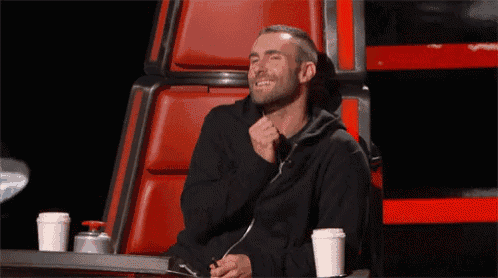 a man in a black hoodie is laughing while sitting in a chair