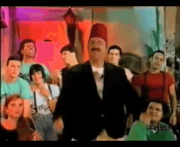 a man with a fez on his head is standing in front of a group of people .