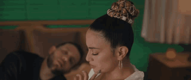 a man laying on a bed next to a woman with a bun