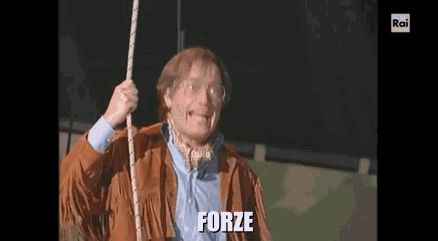 a man in a brown jacket is holding a rope and the word forze is on the screen .