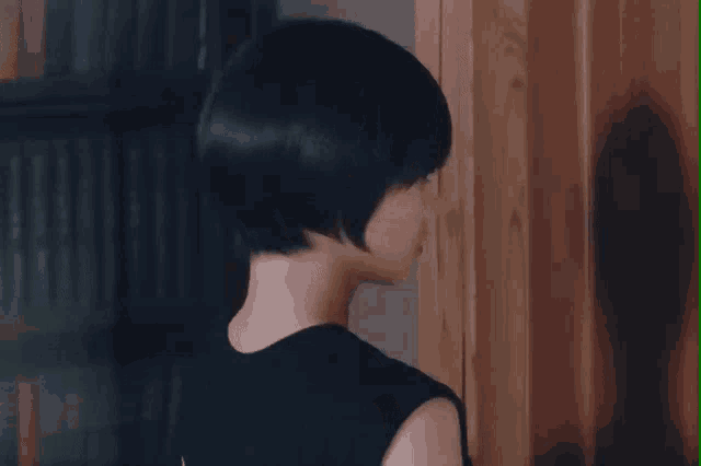 a woman with short black hair is standing in front of a bookcase