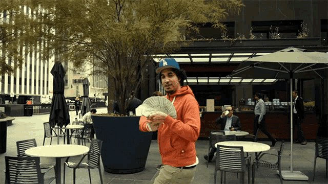 a man holding a fan of money in front of a restaurant