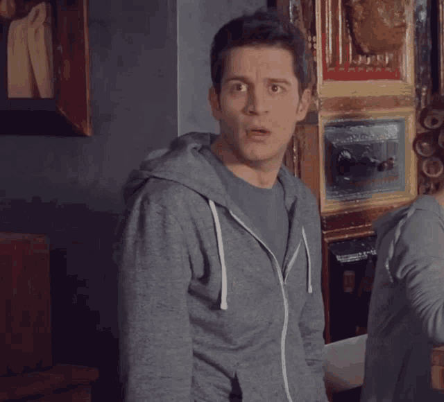 a man with a surprised look on his face wears a grey hoodie