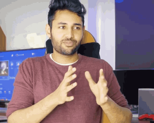 a man in a maroon shirt is sitting in front of a monitor