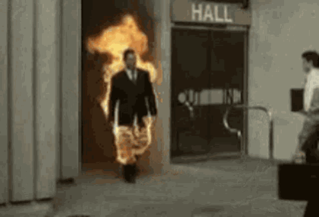 a man in a suit and tie is walking through a doorway with fire coming out of it .