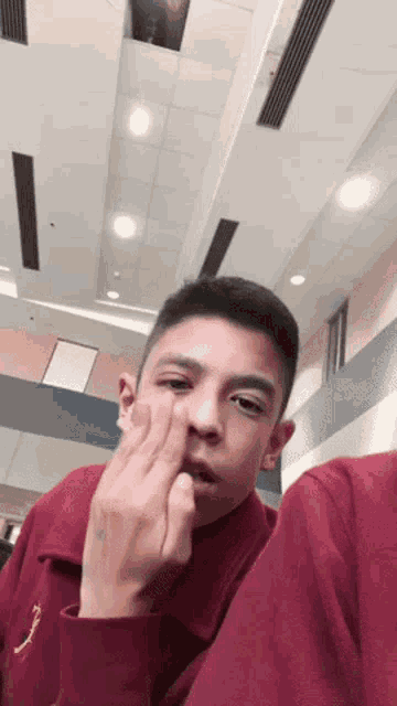 a young man in a maroon shirt is making a funny face while sitting in a room .