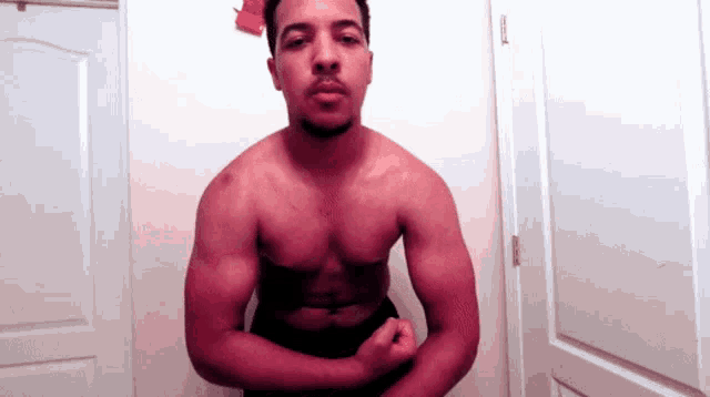 a shirtless man flexing his muscles in front of a white door