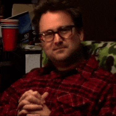 a man wearing glasses and a plaid shirt is sitting in a chair