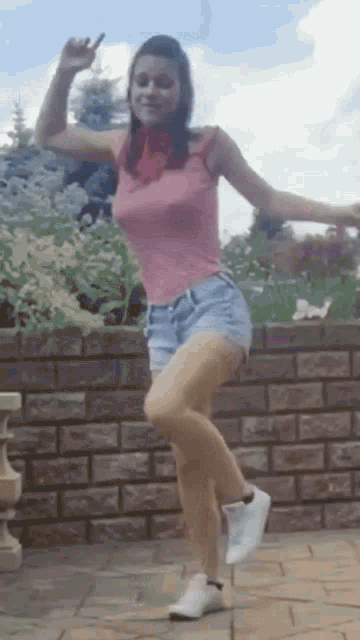 a woman in a pink shirt and shorts is dancing on a sidewalk