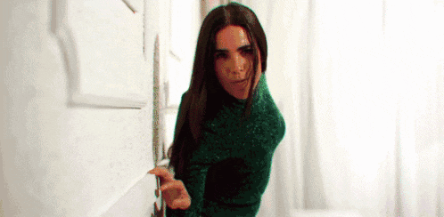 a woman in a green sweater is standing in a doorway .