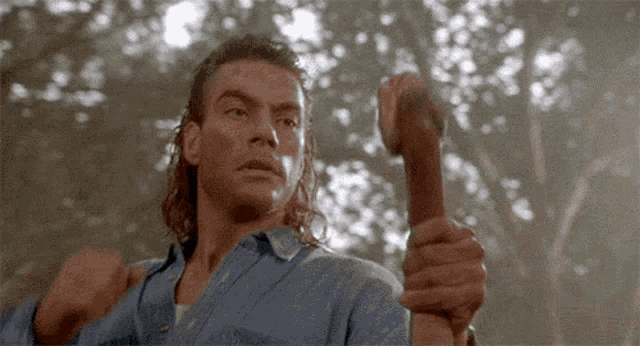 a man in a blue shirt is holding a wooden stick .