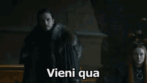 a man in a fur coat is standing next to a woman in a dark room and says vieni qua .