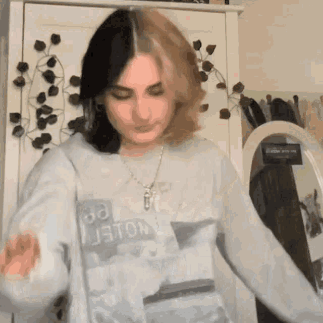 a girl with half black and half blonde hair is standing in front of a mirror wearing a sweatshirt .