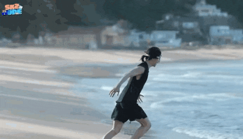 a man in a black tank top and black shorts is running on the beach .