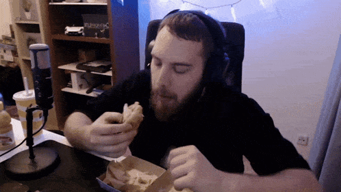 a man wearing headphones is eating a hamburger in front of a microphone