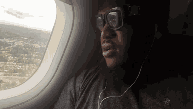 a man wearing sunglasses and ear buds is sitting in an airplane looking out the window .