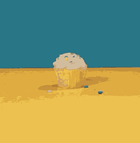 a cupcake with white frosting and colorful sprinkles on a yellow surface
