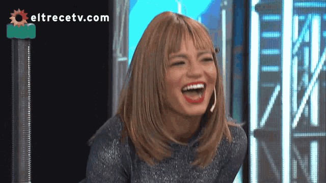 a woman is laughing in front of a screen that says eltrecetv.com on it