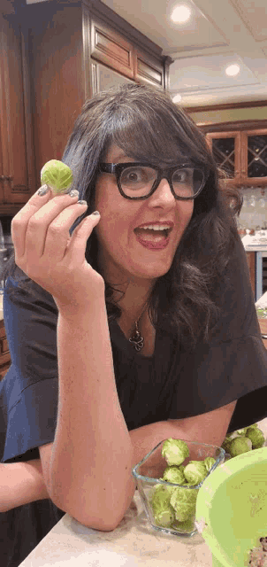 a woman wearing glasses is holding a small vegetable in her hand