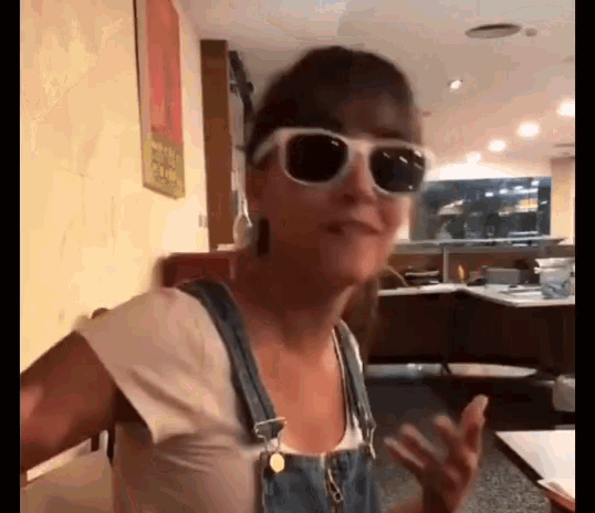 a woman wearing sunglasses and overalls is sitting in a restaurant .