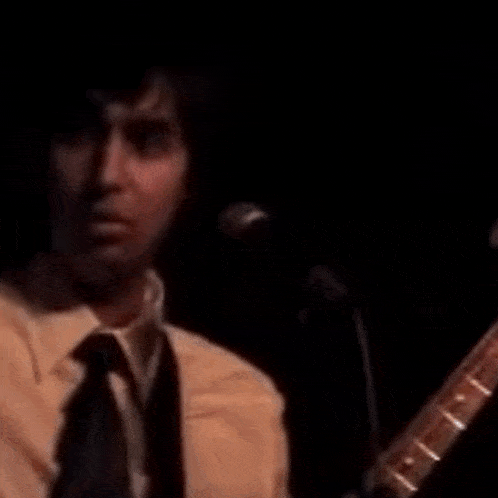a man in a suit and tie is singing into a microphone while holding a guitar .