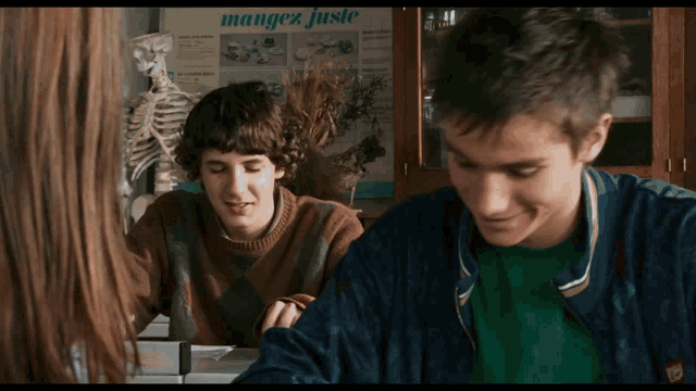 two boys sit at a table in front of a sign that says " mangez juste "