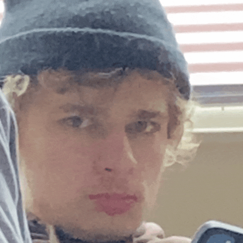 a young man wearing a beanie and holding a cell phone looks at the camera