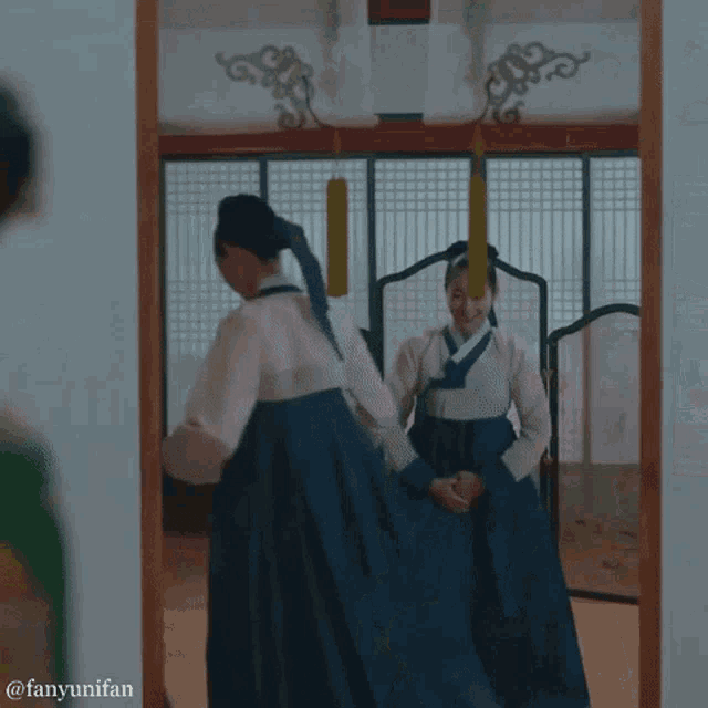 a woman in a traditional korean dress stands in front of a mirror .