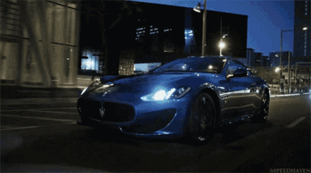 a blue sports car is driving down a street at night