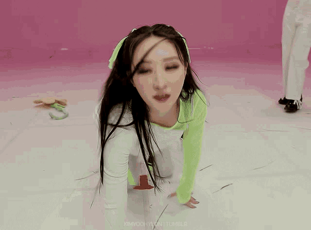 a girl with long black hair is kneeling on the floor in front of a pink wall