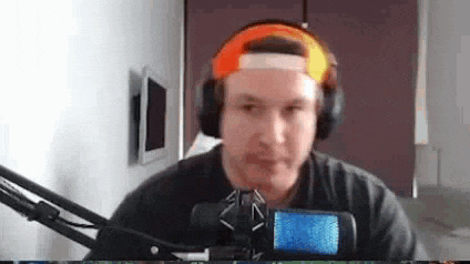 a man wearing headphones and a baseball cap is sitting in front of a microphone .
