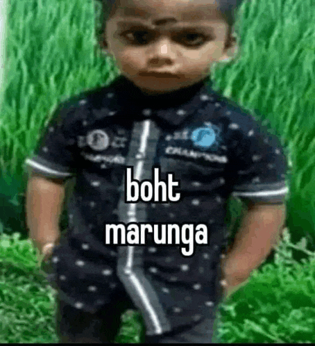 a young boy is standing in a field with his hands in his pockets and wearing a black shirt .