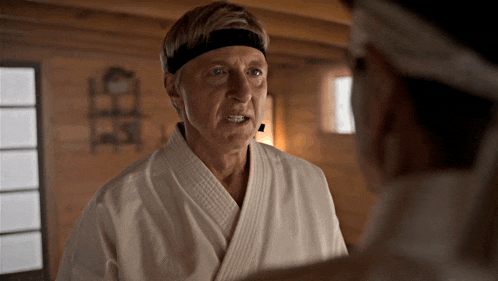 a man in a white karate uniform is talking to another man in a black headband