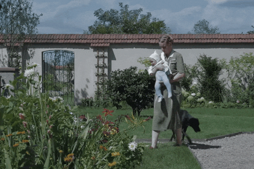 a woman is holding a baby in her arms while walking a dog