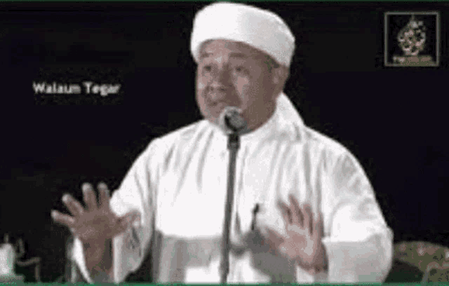 a man in a white robe is standing in front of a microphone and talking into it .