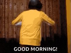 a person in a yellow shirt is standing in front of a curtain and says `` good morning '' .