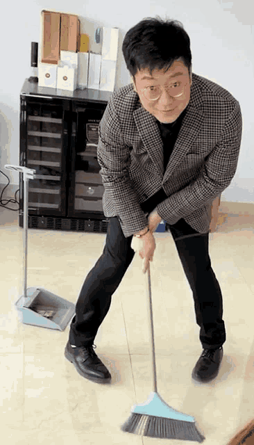 a man in a plaid jacket is sweeping the floor with a blue broom