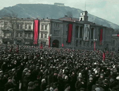 a large crowd of people are gathered in front of a building with a mountain in the background