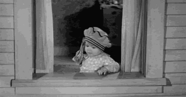a baby is looking out of a window wearing a hat and scarf .