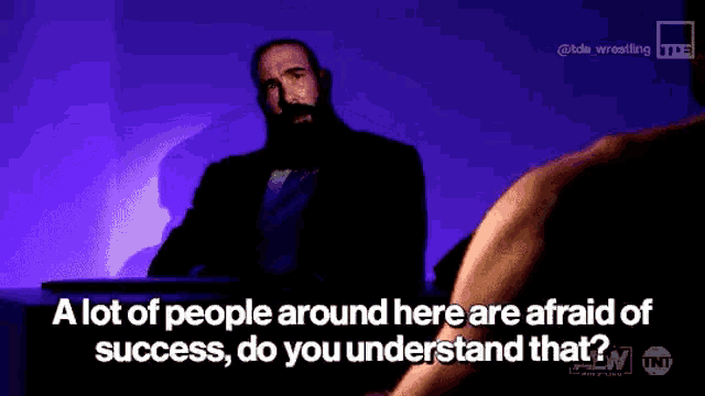 a man with a beard is sitting at a table with a purple background .