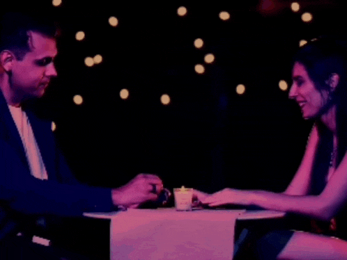 a man and a woman are sitting at a table with a candle in front of them