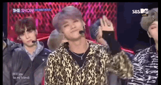 a man in a leopard print shirt is standing in front of a group of young men on a stage ..