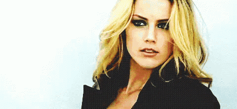 a close up of a woman 's face with long blonde hair and a black jacket .