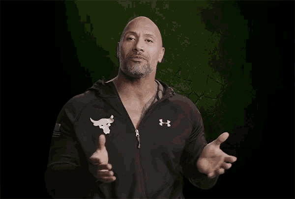 a bald man wearing a black under armour jacket is talking to someone .