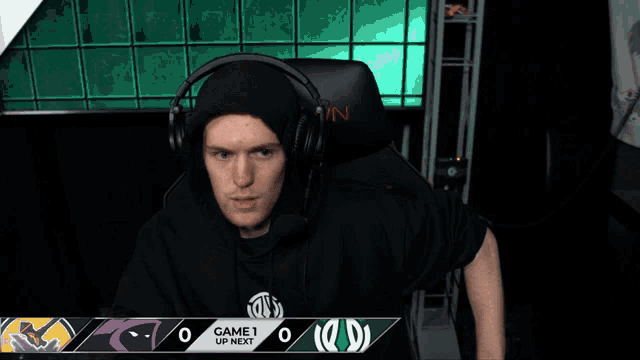 a man wearing headphones sits in front of a scoreboard that says game 1 up next on it