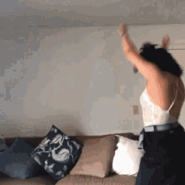 a woman is dancing in front of a couch with pillows on it