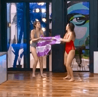 two women in swimsuits are standing next to each other on a wooden floor holding a purple bag .
