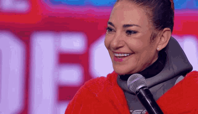 a woman is smiling while holding a microphone in front of a sign that says des