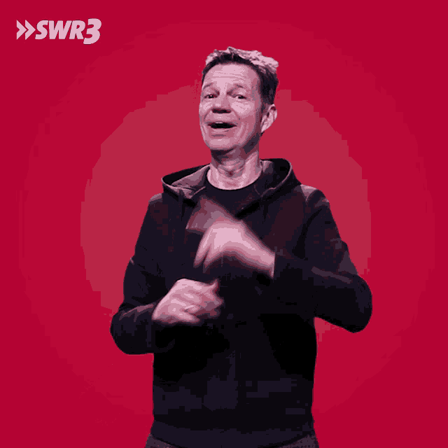 a man in a black jacket is smiling in front of a red background with swr3 written above him
