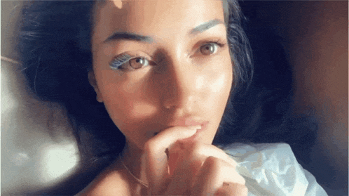 a close up of a woman laying on a bed with her hand on her mouth